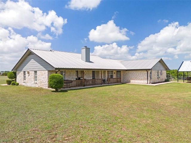 back of property featuring metal roof, stone siding, a lawn, and a chimney