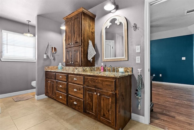 full bath featuring baseboards, a sink, toilet, and double vanity