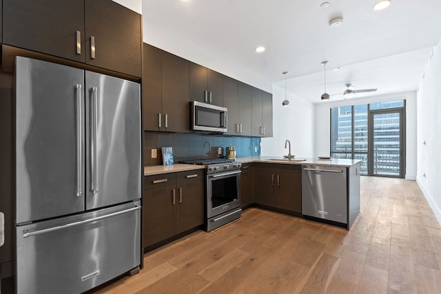 kitchen featuring high quality appliances, hanging light fixtures, a peninsula, light countertops, and a sink