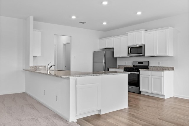 kitchen featuring a peninsula, white cabinetry, appliances with stainless steel finishes, and light stone counters