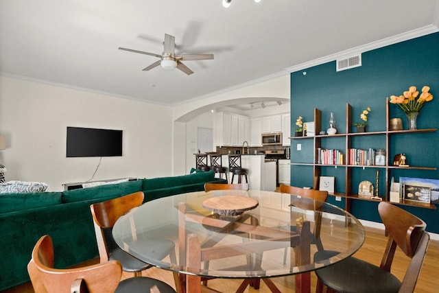 dining space featuring arched walkways, crown molding, visible vents, ceiling fan, and wood finished floors