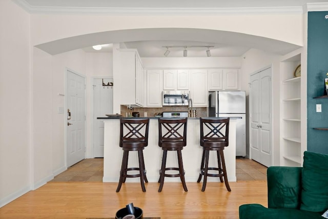 kitchen featuring arched walkways, stainless steel appliances, a kitchen breakfast bar, white cabinets, and dark countertops