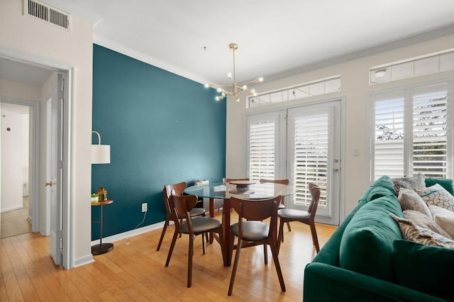 dining room featuring ornamental molding, light wood-style flooring, visible vents, and baseboards