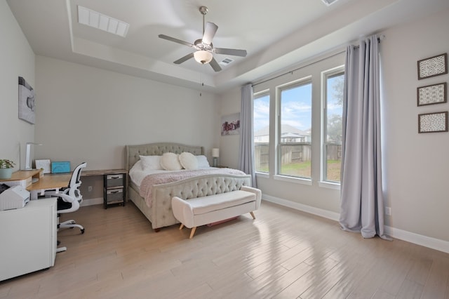 bedroom featuring a tray ceiling, light wood-style flooring, visible vents, and baseboards