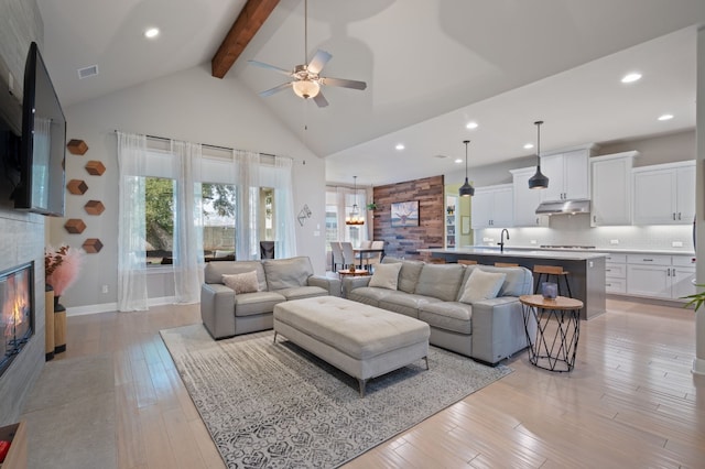 living room featuring visible vents, light wood-style flooring, beamed ceiling, a fireplace, and high vaulted ceiling