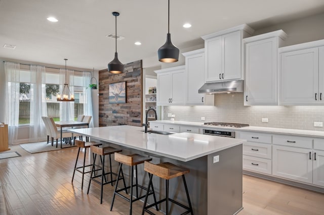 kitchen featuring light countertops, a sink, under cabinet range hood, and an island with sink