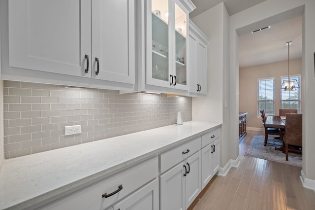 bar featuring pendant lighting, a notable chandelier, light wood finished floors, tasteful backsplash, and baseboards