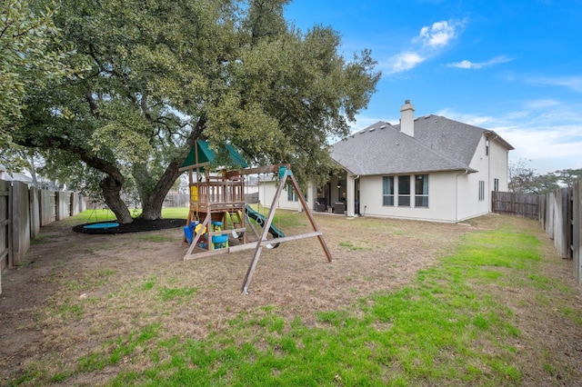 exterior space featuring a fenced backyard, a chimney, roof with shingles, a yard, and a playground
