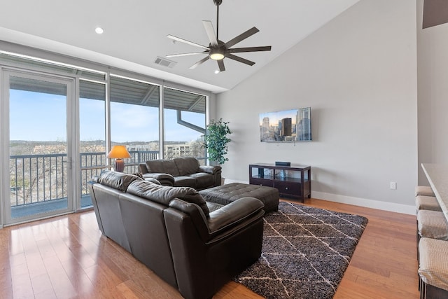 living area featuring baseboards, ceiling fan, wood finished floors, floor to ceiling windows, and high vaulted ceiling