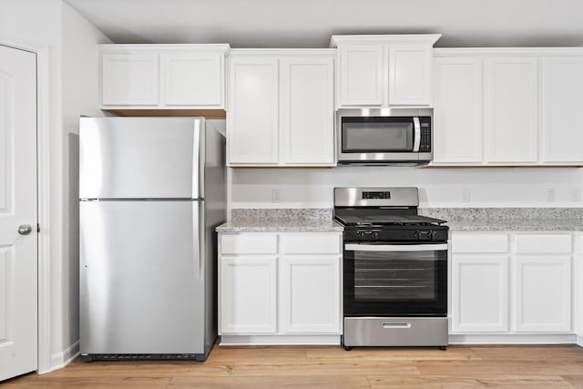 kitchen with stainless steel appliances, light wood-type flooring, white cabinetry, and light stone countertops