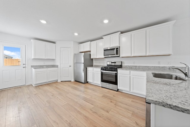 kitchen with light stone counters, stainless steel appliances, light wood-style floors, white cabinetry, and a sink