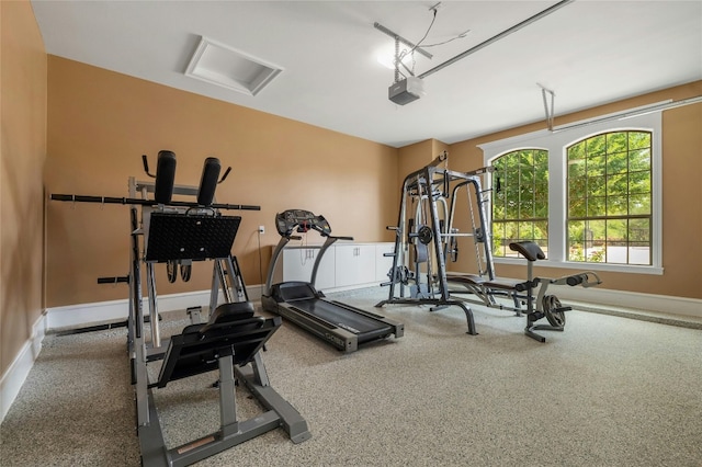 exercise room with a garage, attic access, and baseboards