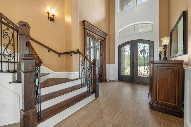 entryway featuring arched walkways, a wainscoted wall, stairway, a high ceiling, and french doors