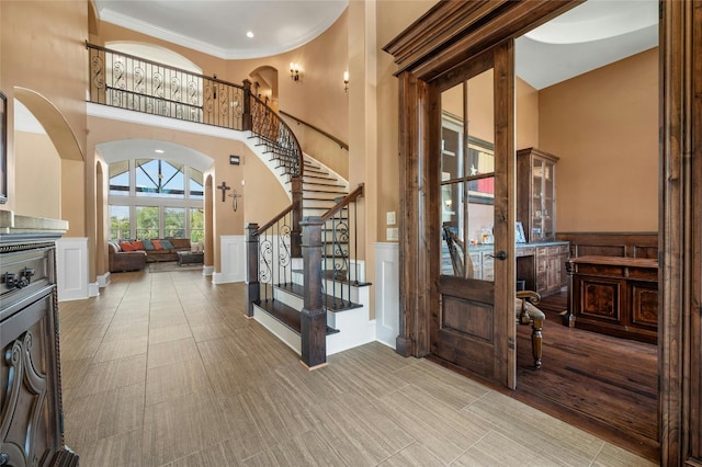 foyer entrance featuring a wainscoted wall, a high ceiling, stairway, and arched walkways