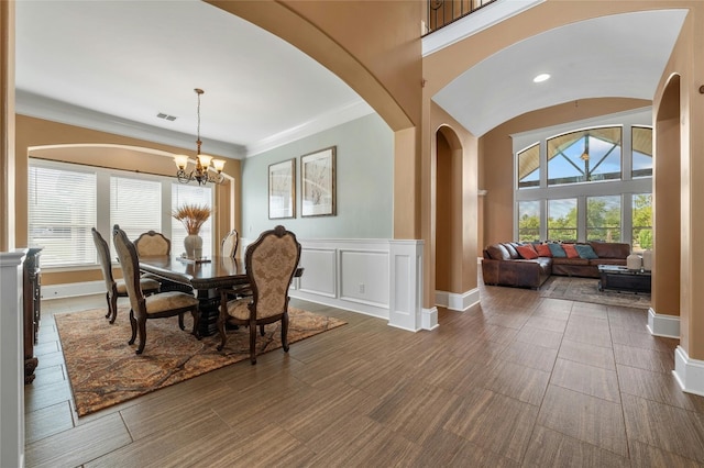 dining space with arched walkways, a decorative wall, wainscoting, an inviting chandelier, and crown molding