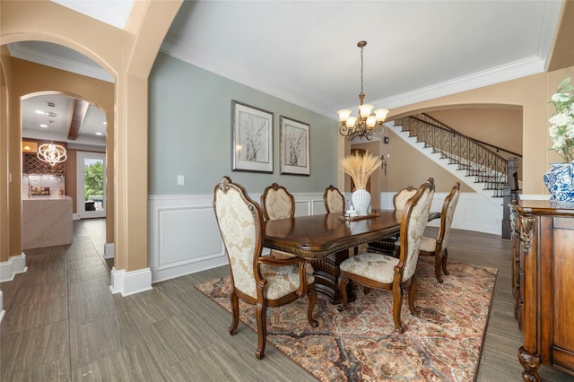 dining space featuring wainscoting, stairway, crown molding, a decorative wall, and a notable chandelier