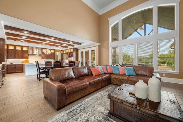 living area with light wood finished floors, baseboards, a high ceiling, crown molding, and beam ceiling