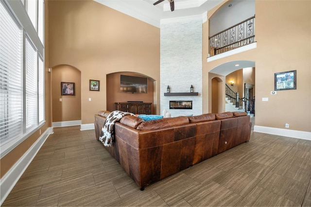 living room with arched walkways, a stone fireplace, a towering ceiling, and baseboards