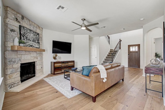 living room featuring stairs, a stone fireplace, light wood-type flooring, and visible vents