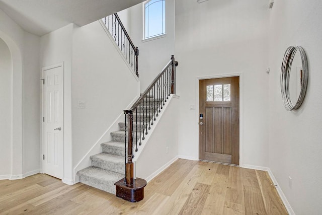 entryway featuring arched walkways, a high ceiling, light wood-style flooring, and baseboards