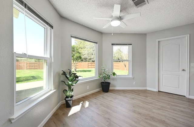 interior space with baseboards, visible vents, a textured ceiling, and light wood finished floors