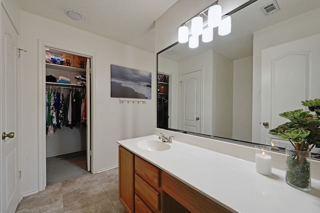 bathroom with a textured ceiling, vanity, a walk in closet, and visible vents