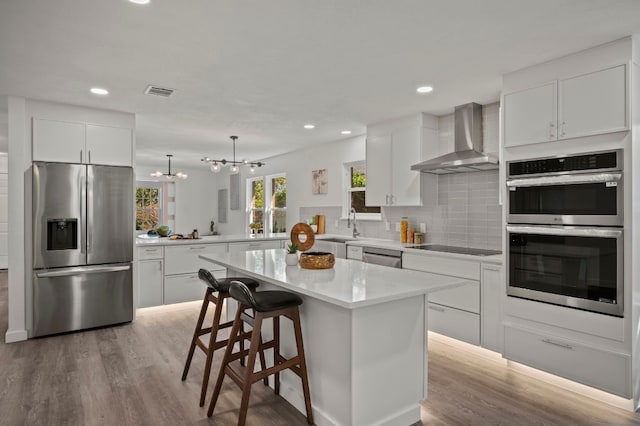 kitchen with visible vents, tasteful backsplash, wood finished floors, appliances with stainless steel finishes, and wall chimney exhaust hood