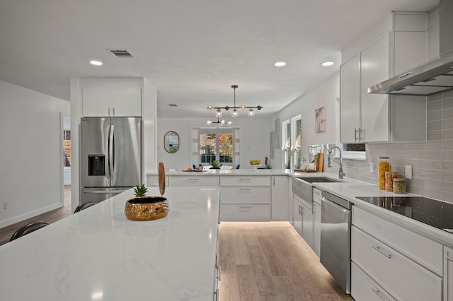 kitchen featuring visible vents, a sink, stainless steel appliances, wall chimney range hood, and tasteful backsplash