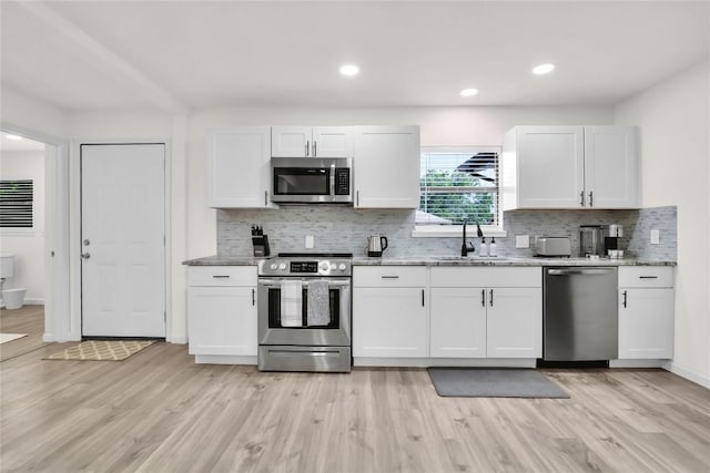 kitchen featuring decorative backsplash, white cabinets, a sink, light wood-style flooring, and stainless steel appliances