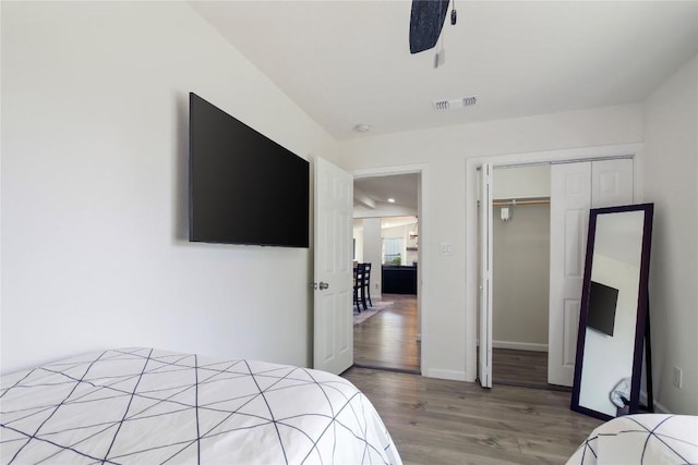 bedroom with ceiling fan, visible vents, wood finished floors, baseboards, and a closet
