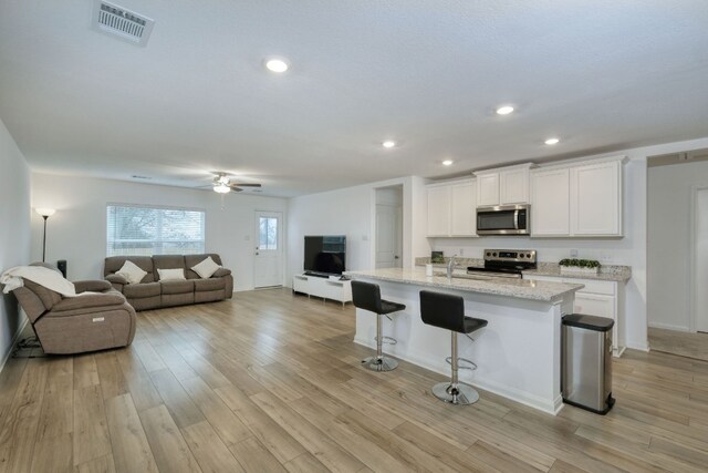 13029 Field Plow Ln, Elgin, TX 78621 - kitchen with stainless steel appliances, open floor plan, white cabinets, a ceiling fan, and a kitchen bar