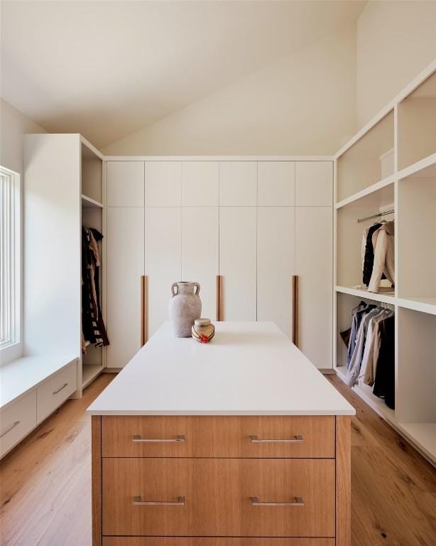 walk in closet with light wood-style floors and vaulted ceiling