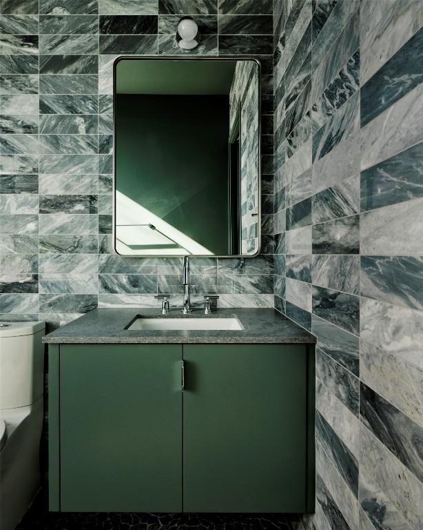 half bathroom featuring backsplash, vanity, toilet, and tile walls