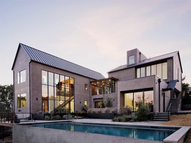 rear view of house with an outdoor pool, a standing seam roof, metal roof, and stairway