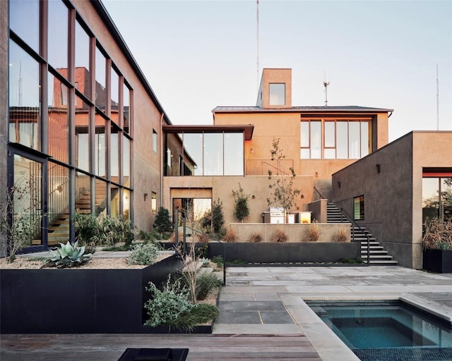 rear view of property with an in ground hot tub, stairway, and stucco siding