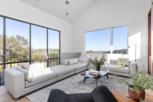 living room with high vaulted ceiling, a wealth of natural light, visible vents, and light wood-style floors