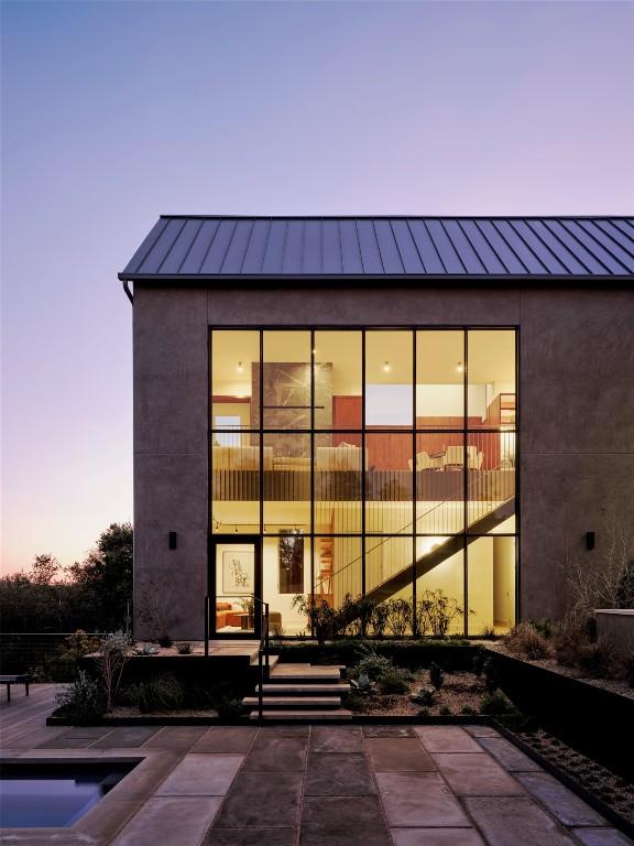 back of house at dusk with a standing seam roof, stucco siding, metal roof, and a patio