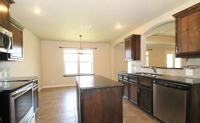 503 W Gemini Ln, Killeen, TX 76542 - kitchen with stainless steel appliances, arched walkways, a kitchen island, tasteful backsplash, and dark tile patterned floors