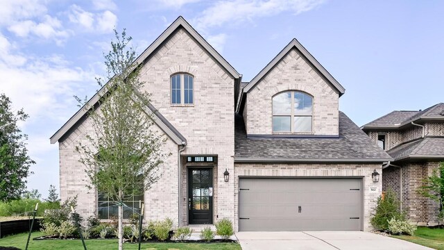 657 Bay Breeze Dr, Kyle, TX 78640 - french country home with brick siding, concrete driveway, an attached garage, and roof with shingles