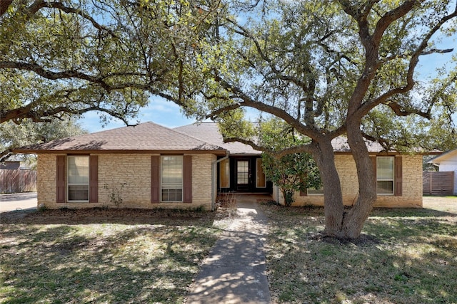 ranch-style home featuring roof with shingles, fence, a front lawn, and brick siding