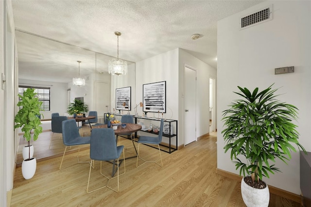 dining space with baseboards, visible vents, light wood-style flooring, a textured ceiling, and a chandelier