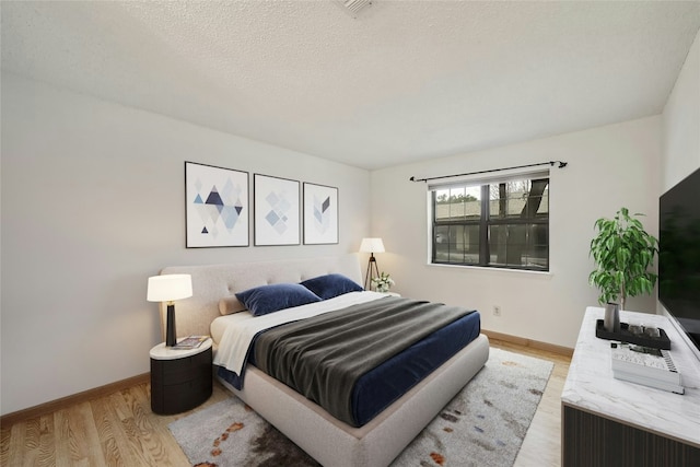 bedroom featuring a textured ceiling, light wood finished floors, and baseboards