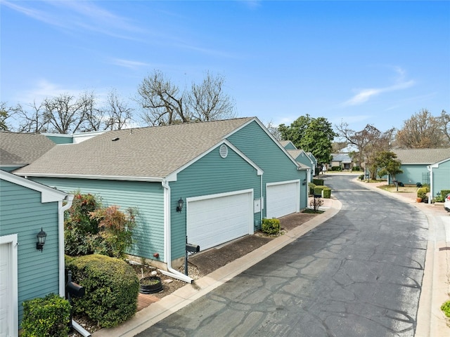 view of property exterior featuring driveway, an attached garage, a residential view, and roof with shingles