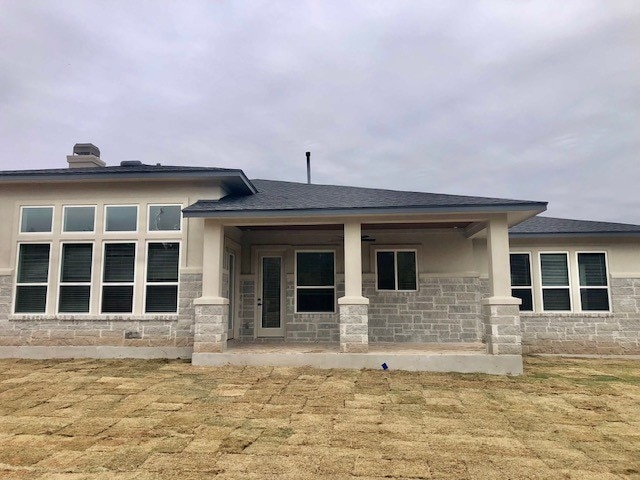 back of property featuring stone siding, a shingled roof, and stucco siding