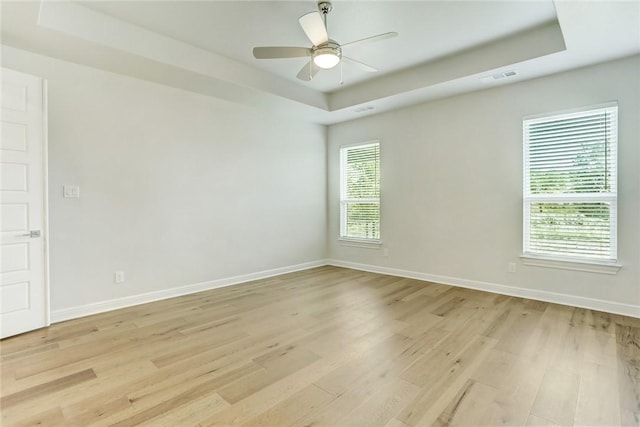 unfurnished room with light wood-style floors, a raised ceiling, visible vents, and baseboards