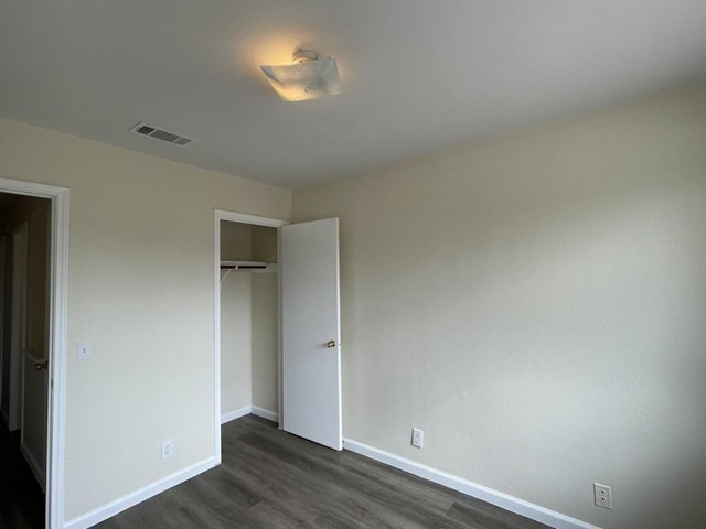 unfurnished bedroom with a closet, dark wood finished floors, visible vents, and baseboards