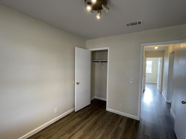 unfurnished bedroom with dark wood-style floors, a closet, visible vents, and baseboards