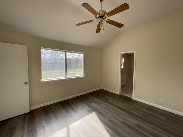 spare room featuring dark wood-type flooring, vaulted ceiling, baseboards, and a ceiling fan