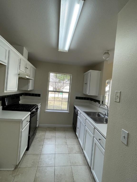 kitchen with light tile patterned floors, black stove, light countertops, white cabinetry, and a sink