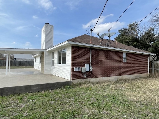 view of property exterior featuring a patio, brick siding, fence, a lawn, and a chimney